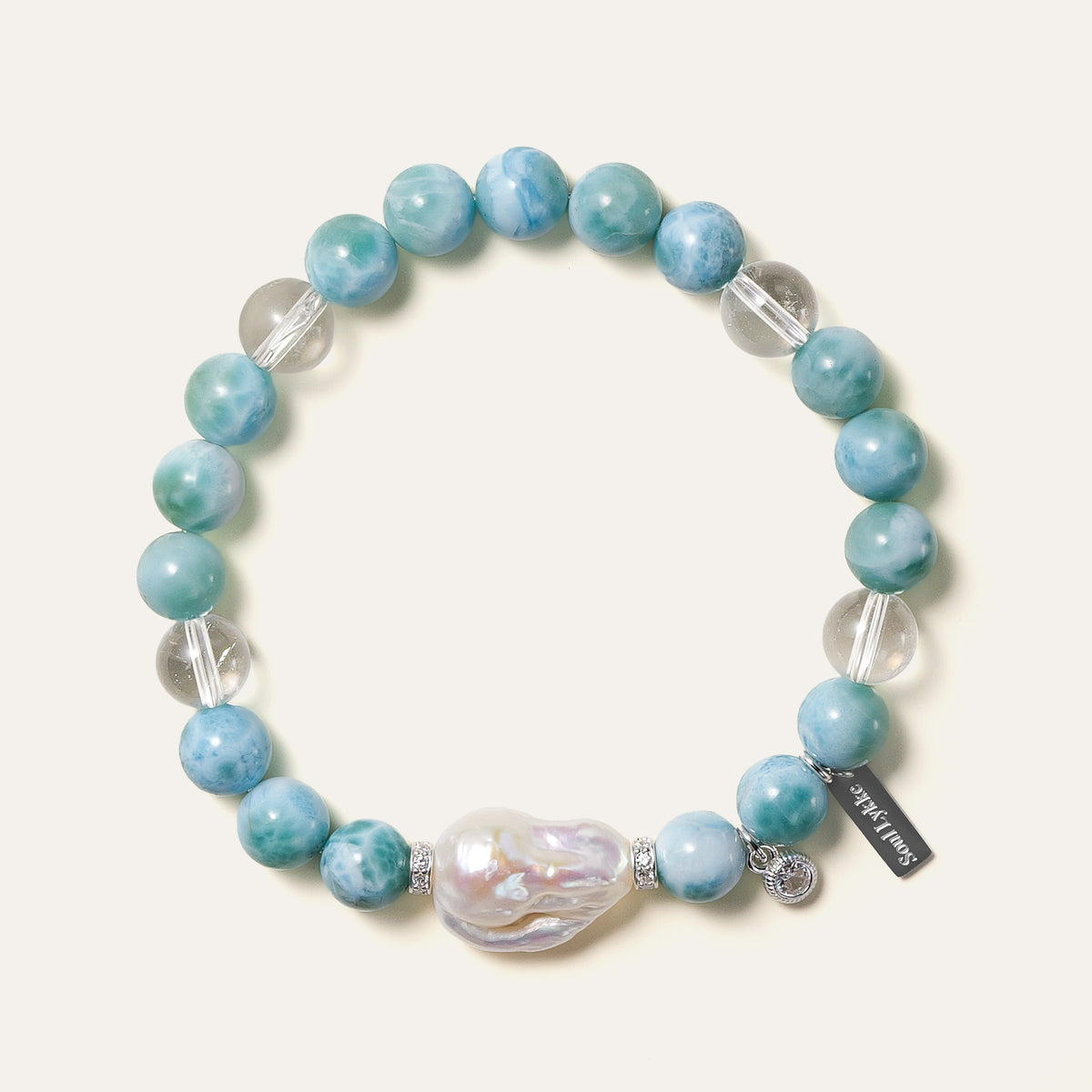 The Marine Veil bracelet by Soul Lykke, featuring an authentic 20mm East Asian baroque pearl centerpiece, surrounded by 8mm AA grade Dominican Larimar, clear quartz, and 925 sterling silver CZ spacers on a neutral background. This is a natural gemstone and healing crystal bracelet by Soul Lykke.