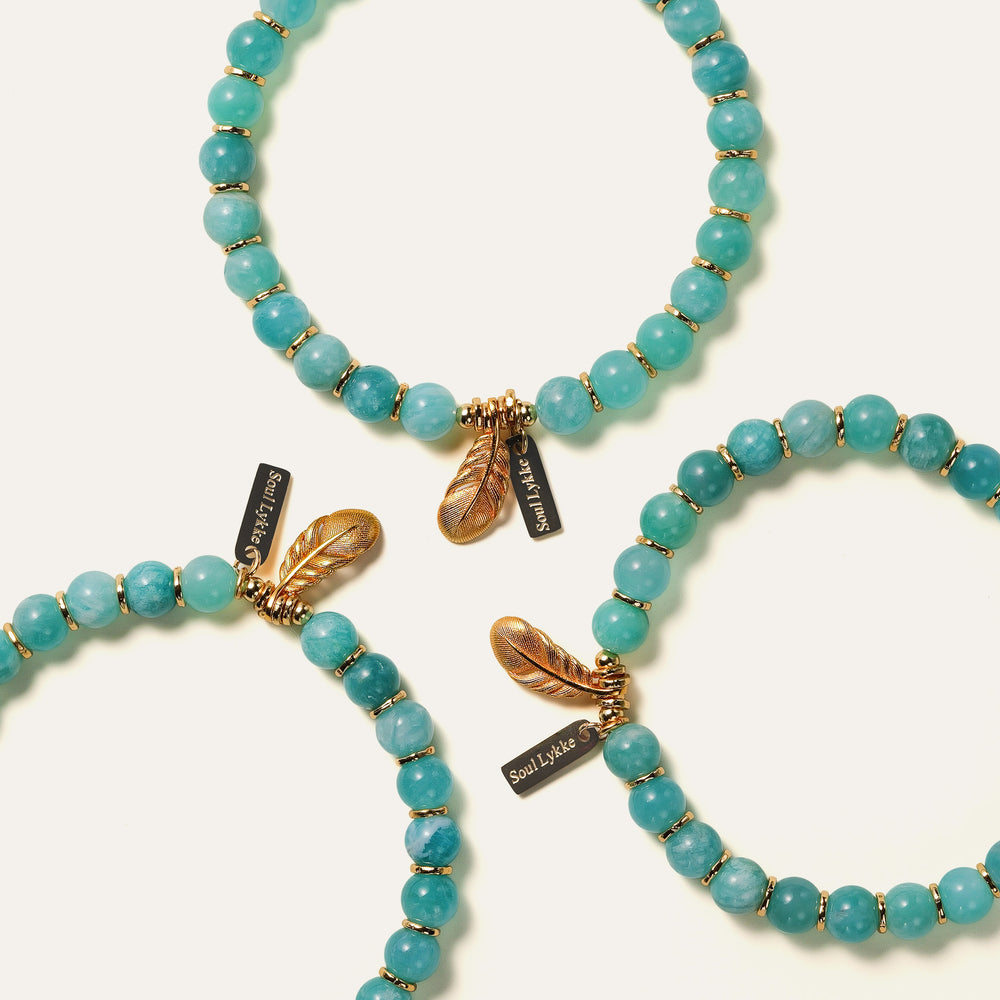 The Tide & Feather bracelet by Soul Lykke, featuring 7mm natural AAA Mozambique icy amazonite beads and a 24K gold-plated sculpted feather charm on a seamless neutral background. This is a natural gemstone and healing crystal bracelet by Soul Lykke.