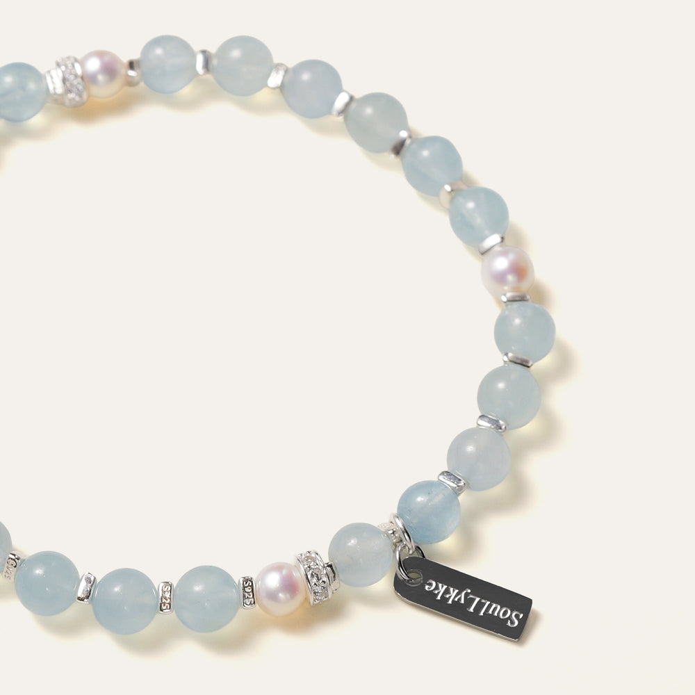The Whispering Cove bracelet by Soul Lykke, featuring 6mm natural AAA Brazilian aquamarine and 5mm Japanese Akoya pearls with 925 sterling silver geometric spacers on a seamless background. This is a natural gemstone and healing crystal bracelet by Soul Lykke.