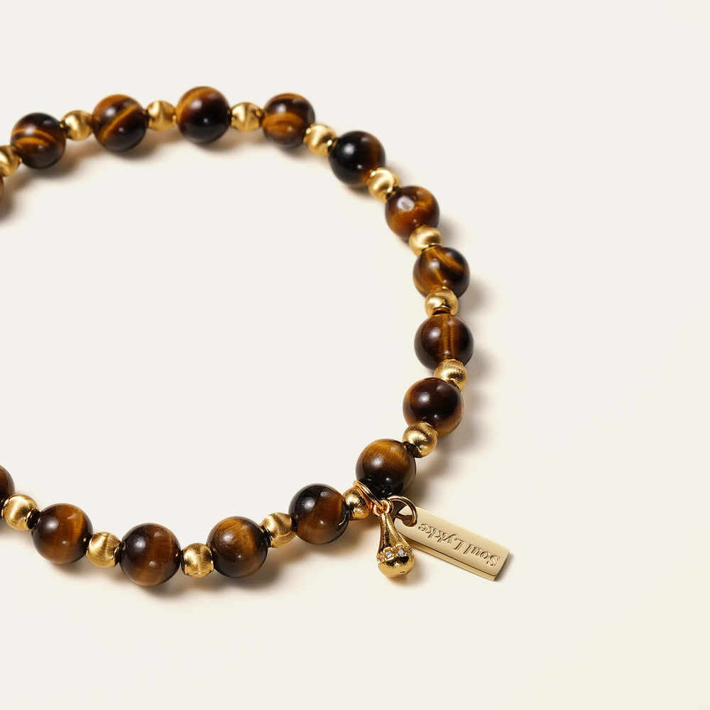The Golden Glaze bracelet by Soul Lykke, featuring 6mm natural AAA South African Tiger's Eye beads and a delicate 24K gold-plated teardrop charm on a neutral background. This is a natural gemstone and healing crystal bracelet by Soul Lykke.