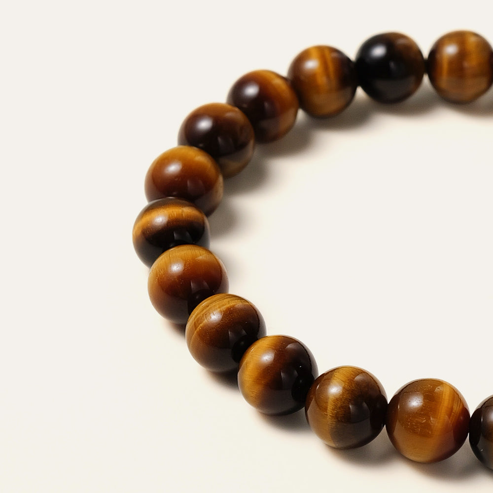 The Core Essential bracelet by Soul Lykke, featuring ethically sourced 8mm natural AAA Tiger's Eye beads from South Africa and a single engraved 14K gold PVD surgical steel signature bead on a seamless neutral background. This is a natural gemstone and healing crystal bracelet by Soul Lykke.
