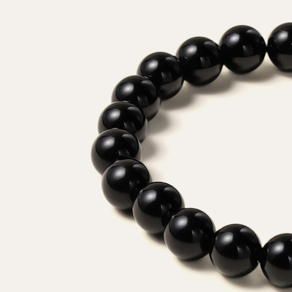 Macro detail of 8mm pure black obsidian gemstone beads, showcasing a highly uniform and glossy texture shaped from rapidly-cooled volcanic glass, exceptionally free of major impurities.