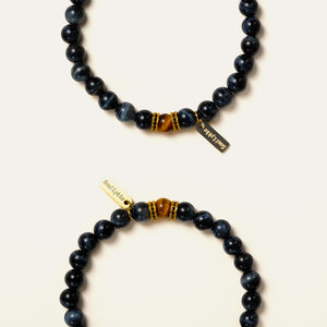 Two natural Blue Tiger's Eye bracelets stacked, highlighting their silky dark blue cat-eye sheen and gold accents.