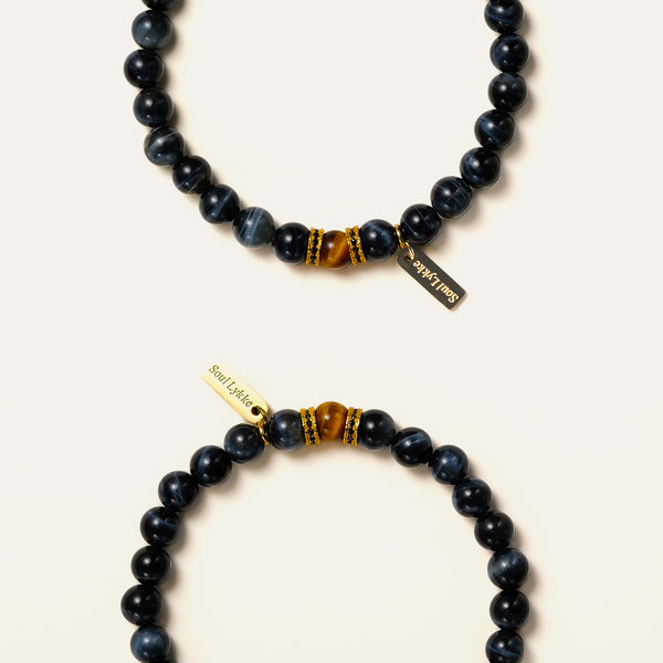 Two natural Blue Tiger's Eye bracelets stacked, highlighting their silky dark blue cat-eye sheen and gold accents.