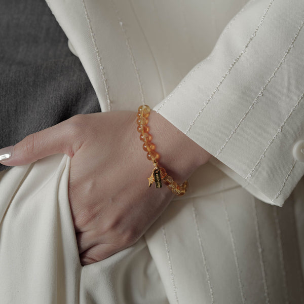 Effortless demi-fine jewelry styling featuring a premium natural Citrine bracelet worn by a model in a white blazer, highlighting the 14K gold PVD surgical steel signature tag.