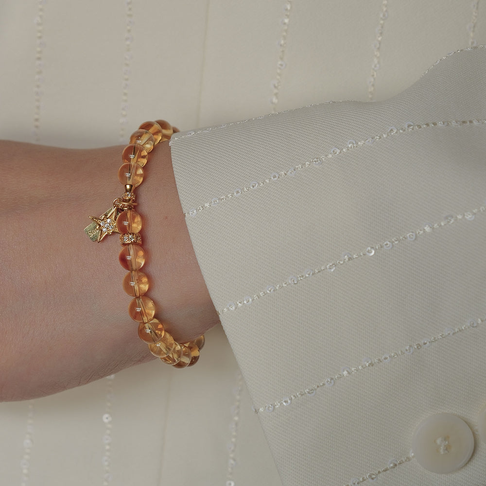 Top-down view of the Soul Lykke Guiding Star bracelet on a neutral background, featuring 6mm AAA Brazil Citrine beads, a 24k gold-plated North Star charm with CZ-pavé accents, and a 14K gold PVD signature tag. This is a natural gemstone and healing crystal bracelet by Soul Lykke.