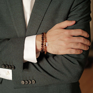 Close-up of a dark suit styling layered Soul Lykke dense-inclusion Black Gold Super Seven bracelets for a commanding presence.