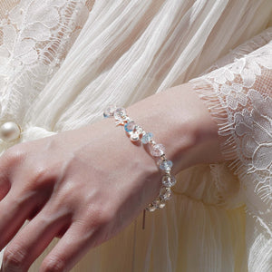 A woman wearing the Glacial Glint bracelet by Soul Lykke with an elegant white lace dress. Featuring 7.5mm faceted AAA Brazilian clear quartz and sky blue topaz, this premium crystal jewelry showcases eye-clean clarity and a brilliant three-dimensional fire.