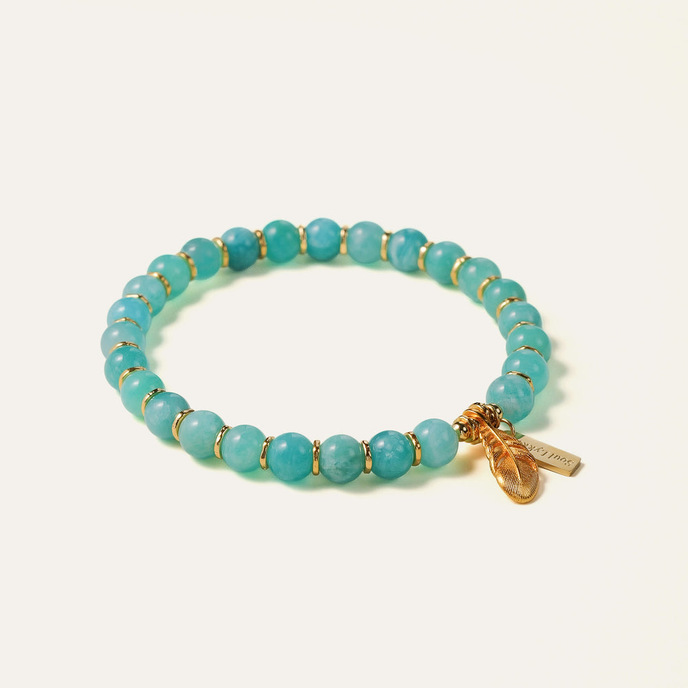 The Tide & Feather bracelet by Soul Lykke, featuring 7mm natural AAA Mozambique icy amazonite beads and a 24K gold-plated sculpted feather charm on a seamless neutral background. This is a natural gemstone and healing crystal bracelet by Soul Lykke.