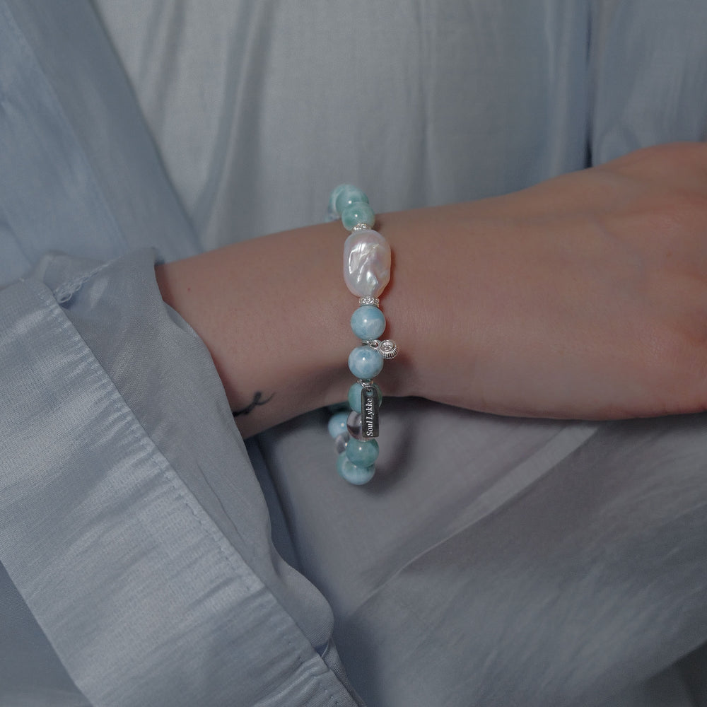 The Marine Veil bracelet by Soul Lykke, featuring an authentic 20mm East Asian baroque pearl centerpiece, surrounded by 8mm AA grade Dominican Larimar, clear quartz, and 925 sterling silver CZ spacers on a neutral background. This is a natural gemstone and healing crystal bracelet by Soul Lykke.