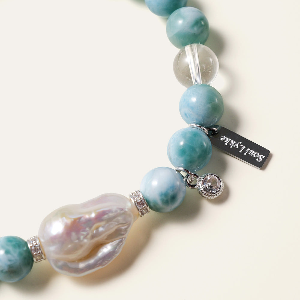 The Marine Veil bracelet by Soul Lykke, featuring an authentic 20mm East Asian baroque pearl centerpiece, surrounded by 8mm AA grade Dominican Larimar, clear quartz, and 925 sterling silver CZ spacers on a neutral background. This is a natural gemstone and healing crystal bracelet by Soul Lykke.