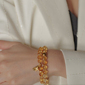 Two glowing honey-gold Citrine crystal bracelets layered gracefully on a woman's wrist, accentuating the natural color zoning of the unheated Brazil stones paired with 24k gold-plated 925 silver accents.