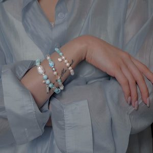 Model wearing a light blue shirt, elegantly styling the Soul Lykke Marine Veil bracelet featuring an 8mm AA Dominican Larimar and a 20mm Baroque Pearl, beautifully layered with the 6mm Marine Tear Larimar and pearl bracelet.