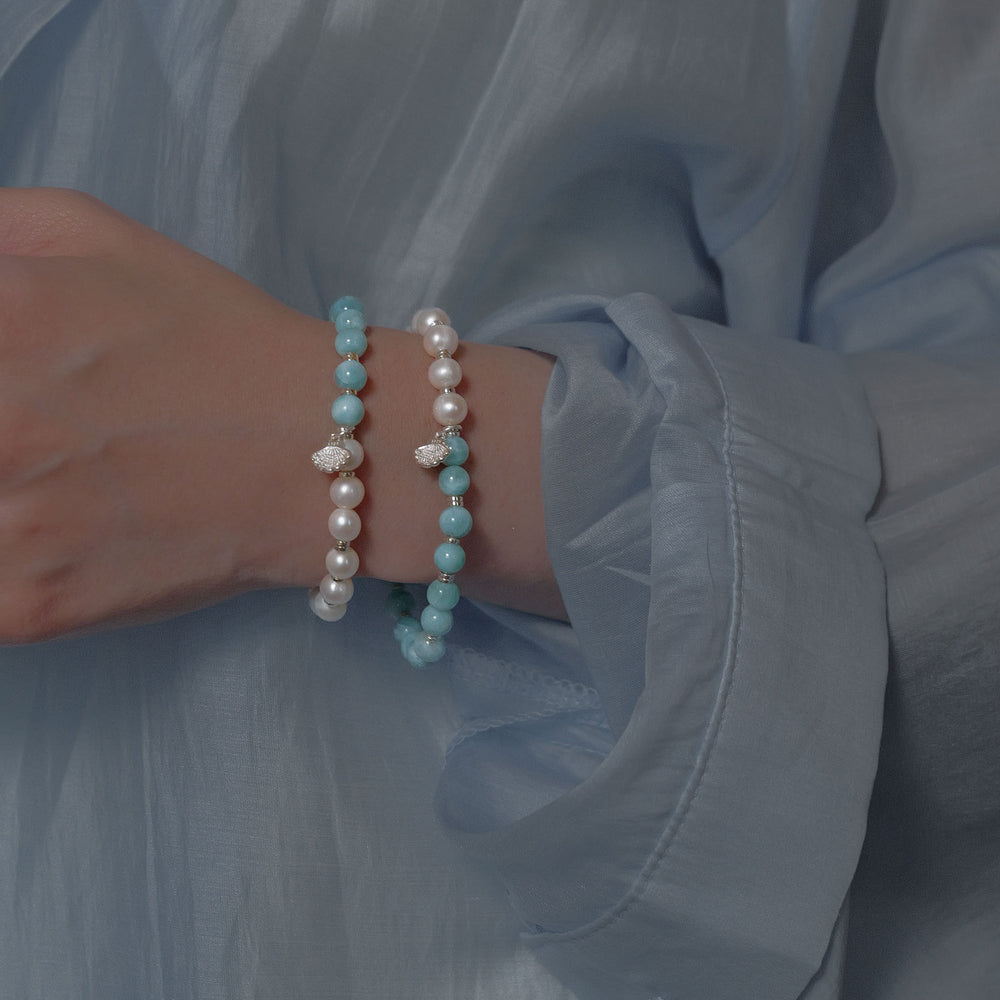 Top view of The Marine Tear artisan bracelet by Soul Lykke, featuring a half-and-half design of 6mm AA grade Dominican Larimar and natural freshwater pearls with a silver seashell charm. This is a natural gemstone and healing crystal bracelet by Soul Lykke.
