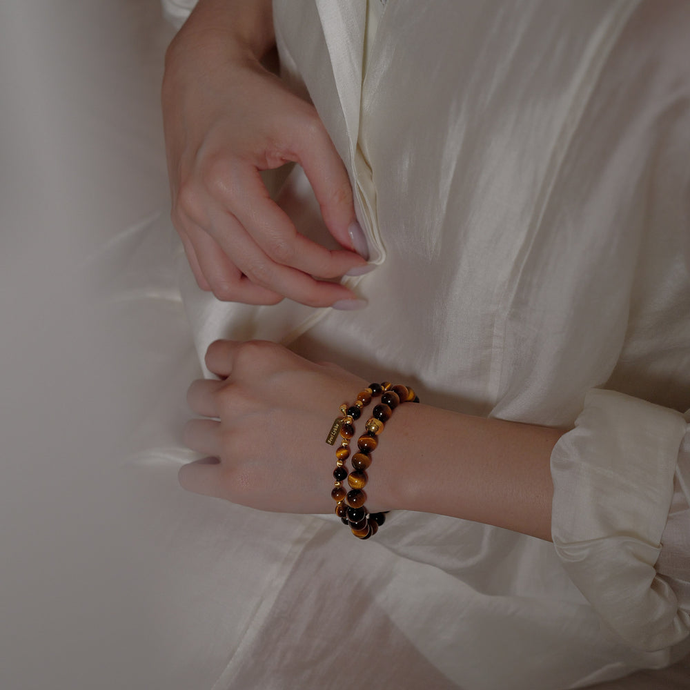 The Core Essential bracelet by Soul Lykke, featuring ethically sourced 8mm natural AAA Tiger's Eye beads from South Africa and a single engraved 14K gold PVD surgical steel signature bead on a seamless neutral background. This is a natural gemstone and healing crystal bracelet by Soul Lykke.