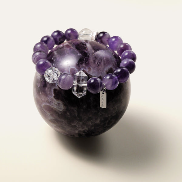 Soul Lykke Lucid Dreamer bracelet styled on a large amethyst sphere, highlighting the protective energy of high-grade 10.5mm chevron amethyst and clear quartz.