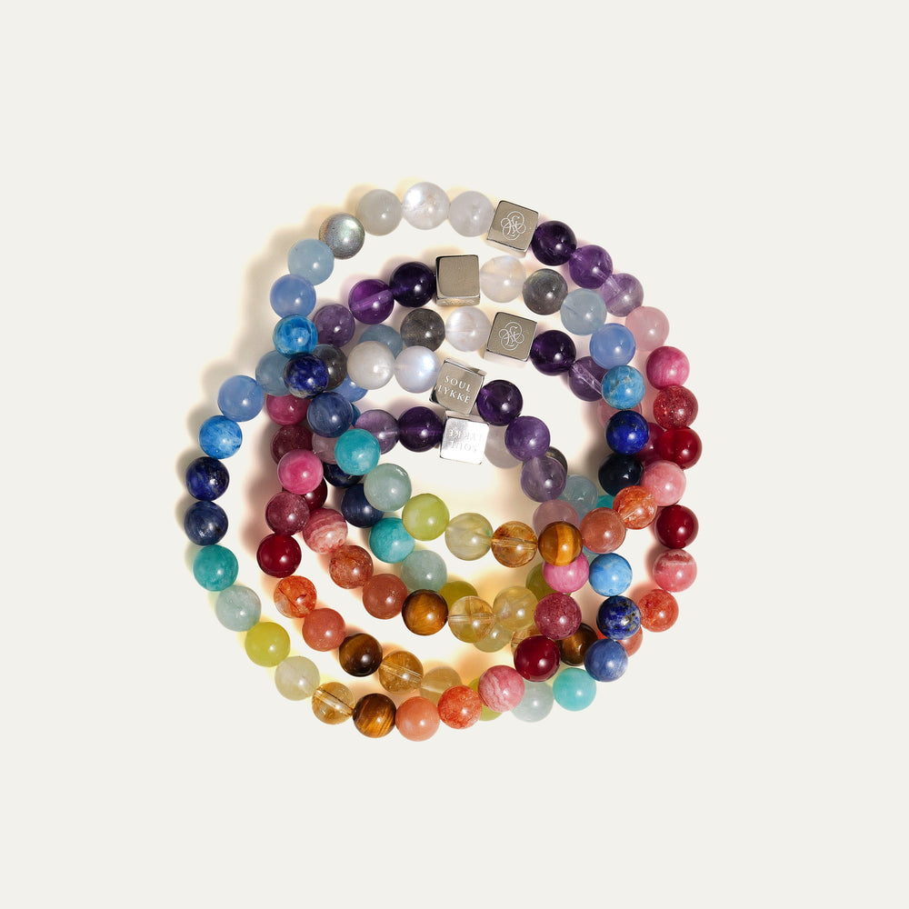 The Earth’s Palette flagship bracelet by Soul Lykke. A museum-grade wearable mineral collection featuring 25 distinct 8mm natural gemstones arranged in a seamless chromatic rainbow gradient, accented by a white gold PVD square signature bead. This is a healing crystal bracelet by Soul Lykke.