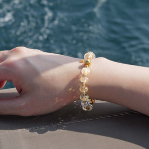 Close-up of a faceted Citrine and Clear Quartz demi-fine bracelet against a deep blue ocean, highlighting the dazzling 24k gold-plated accents.