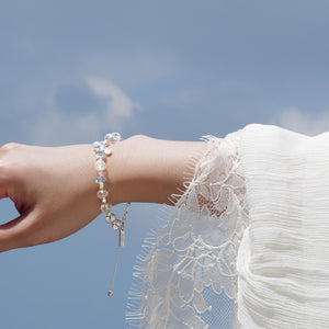 The faceted blue topaz and clear quartz healing bracelet held gracefully against a clear sky, highlighting the 925 sterling silver star charm and hypoallergenic white gold PVD signature tag. Designed to amplify mental clarity and empower authentic communication.