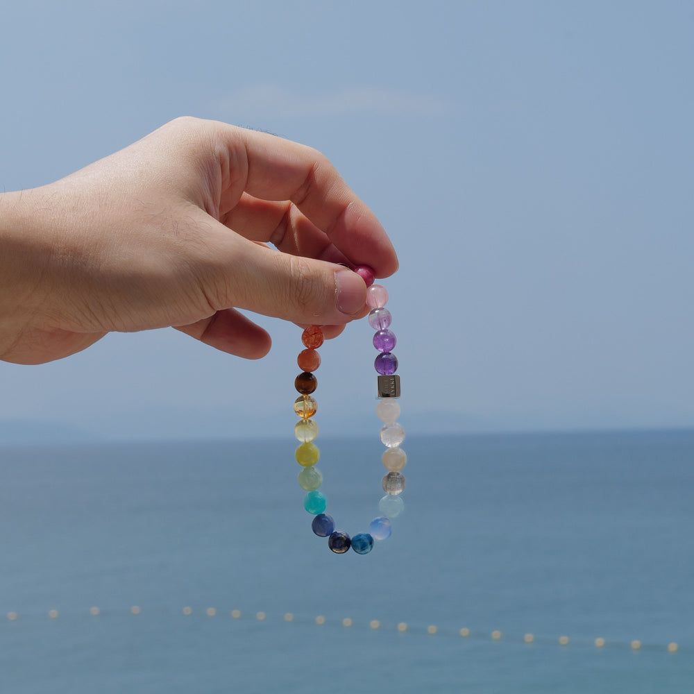 The Earth’s Palette flagship bracelet by Soul Lykke. A museum-grade wearable mineral collection featuring 25 distinct 8mm natural gemstones arranged in a seamless chromatic rainbow gradient, accented by a white gold PVD square signature bead. This is a healing crystal bracelet by Soul Lykke.