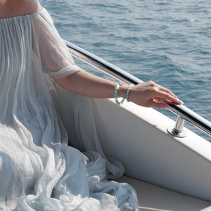 Model relaxing on a boat, wearing the Marine Veil bracelet with a luminous 20mm Baroque Pearl and clear Quartz, elegantly layered with 6mm Dominican Larimar for a tranquil, water-element inspired summer style.