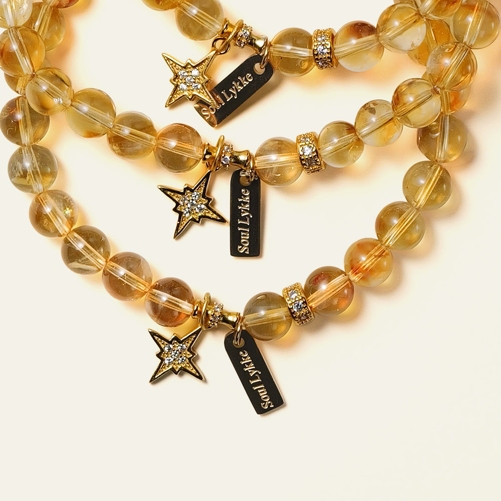 Top-down view of the Soul Lykke Guiding Star bracelet on a neutral background, featuring 6mm AAA Brazil Citrine beads, a 24k gold-plated North Star charm with CZ-pavé accents, and a 14K gold PVD signature tag. This is a natural gemstone and healing crystal bracelet by Soul Lykke.