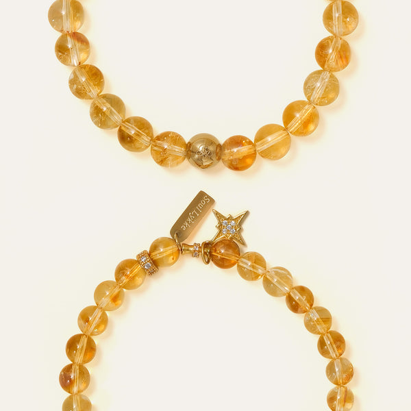 Comparison detail shot showing two premium Honey Citrine bracelets: one with a gold PVD signature bead and one with an engraved Soul Lykke brand tag and star charm, both featuring high clarity natural gemstones.