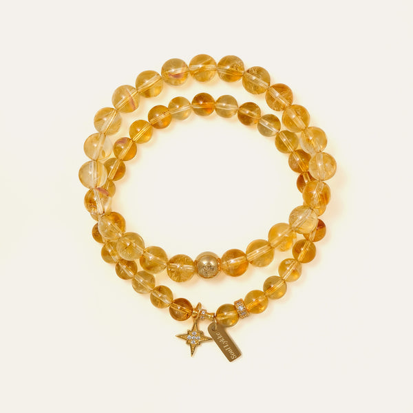 Two stacked premium natural Honey Citrine bracelets, one with an engraved Soul Lykke brand tag and 14K gold star charm with clear crystals, designed for conscious manifestors seeking abundance and success.