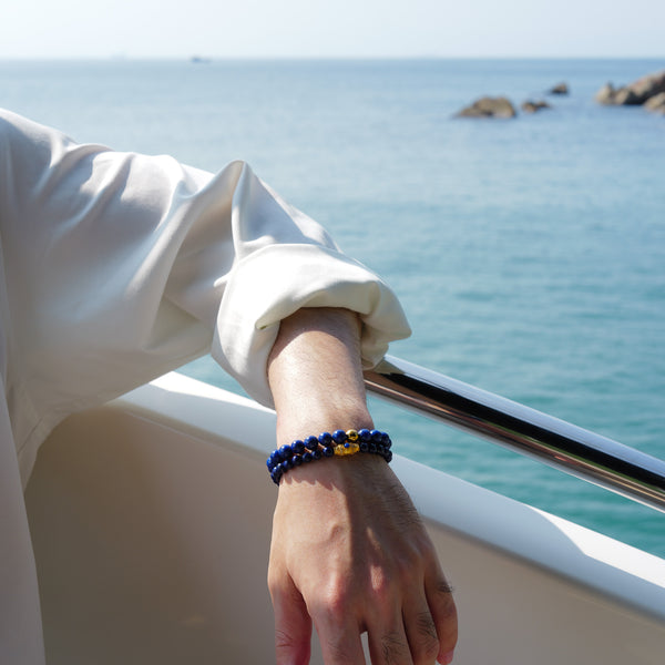 Sophisticated men's styling featuring a layered stack of natural AAA-grade Afghan Lapis Lazuli bracelets. The deeply saturated royal blue stones evoke a pristine night sky, empowering the wearer with intellectual sovereignty and clear expression.