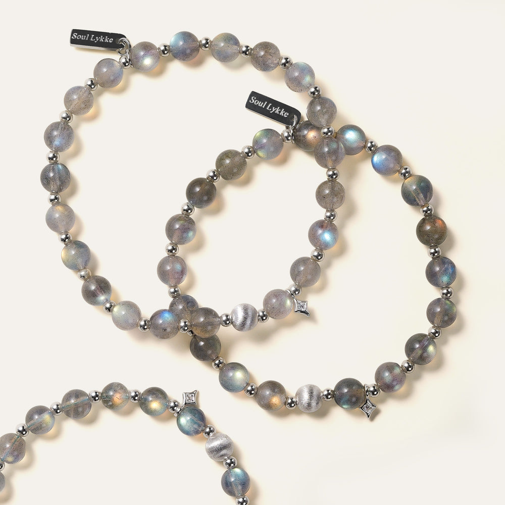Top-down view of the Soul Lykke Inner Universe bracelet, featuring 6.5-7mm natural AAA-grade Madagascar Labradorite with vivid spectral flashes, accented by 925 sterling silver hardware and a white gold PVD surgical steel tag. This is a natural gemstone and healing crystal bracelet by Soul Lykke.