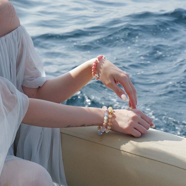 Model on a yacht styling the Monet pastel gemstone bracelet on one wrist, paired with layered Citrine and Rhodochrosite bracelets on the other.