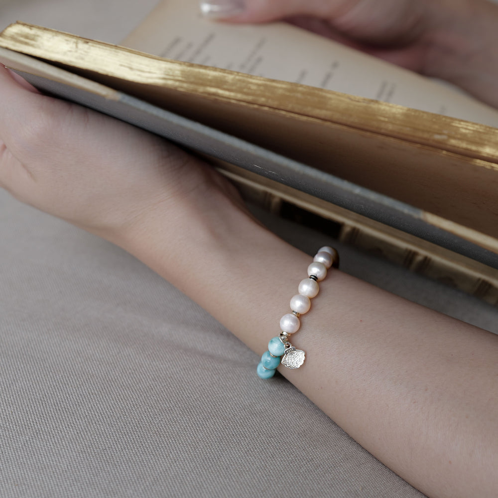 Top view of The Marine Tear artisan bracelet by Soul Lykke, featuring a half-and-half design of 6mm AA grade Dominican Larimar and natural freshwater pearls with a silver seashell charm. This is a natural gemstone and healing crystal bracelet by Soul Lykke.