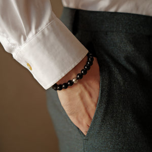 A person elegantly wearing the 8mm natural black obsidian healing bracelet with a tailored shirt and trousers. Anchoring the Root Chakra, this grounding crystal jewelry forms a protective shield to dissolve tension and quiet mental noise.