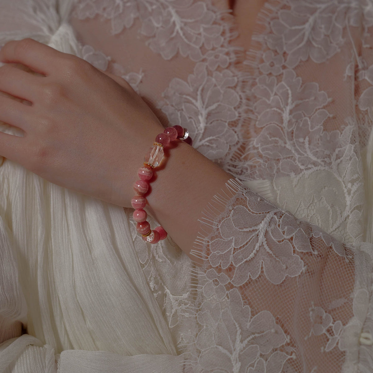 The Rose & Starlight natural Lace Rhodochrosite and Strawberry Quartz bracelet worn gracefully on the wrist against delicate white lace.