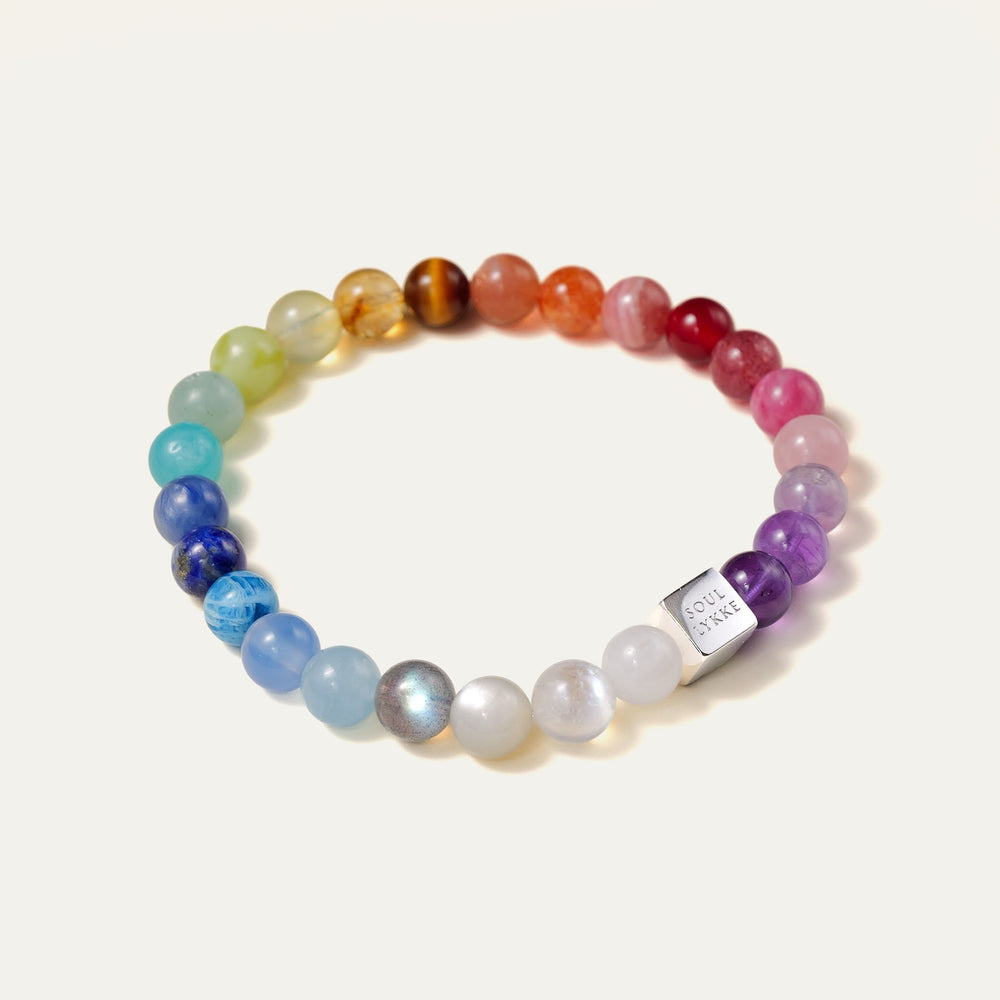 The Earth’s Palette flagship bracelet by Soul Lykke. A museum-grade wearable mineral collection featuring 25 distinct 8mm natural gemstones arranged in a seamless chromatic rainbow gradient, accented by a white gold PVD square signature bead. This is a healing crystal bracelet by Soul Lykke.
