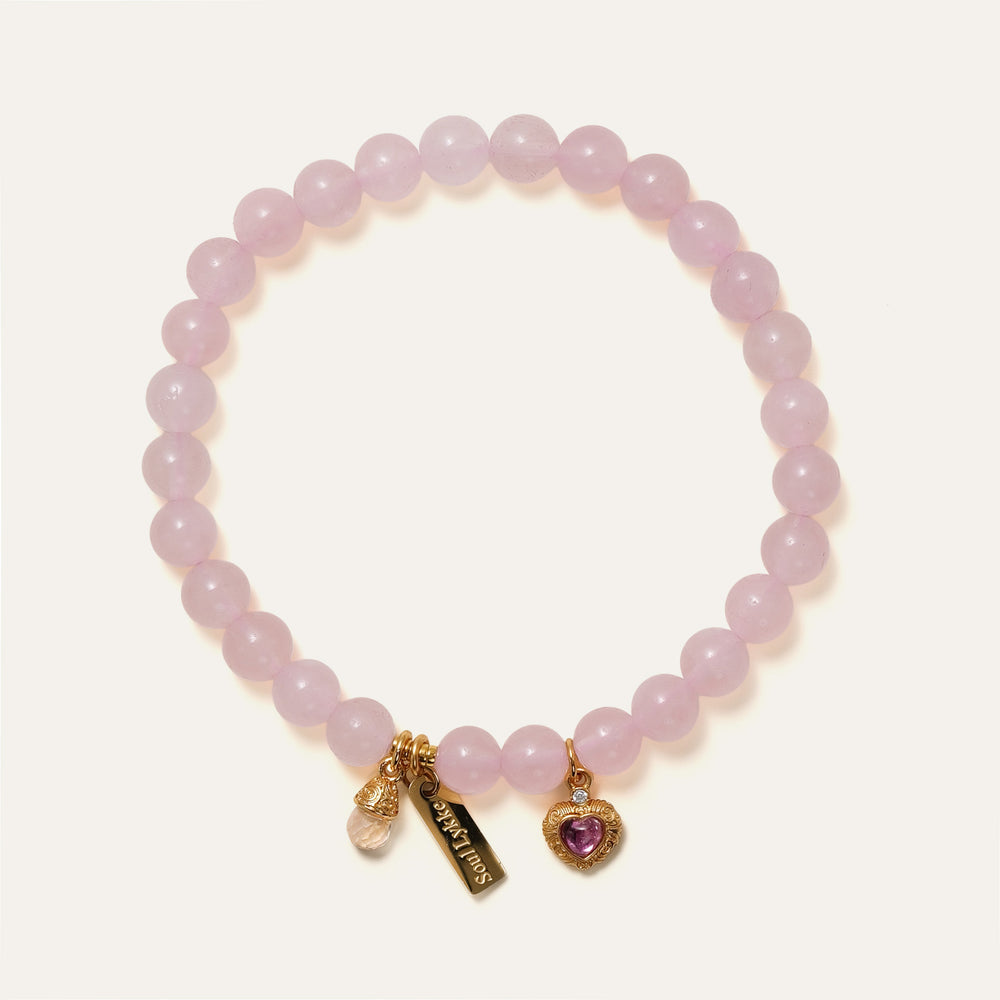 Soft Bloom bracelet by Soul Lykke featuring 6mm AAA Sakura Pink Rose Quartz, a pink tourmaline filigree heart, and a 14K gold PVD signature tag. This is a natural gemstone and healing crystal bracelet by Soul Lykke.