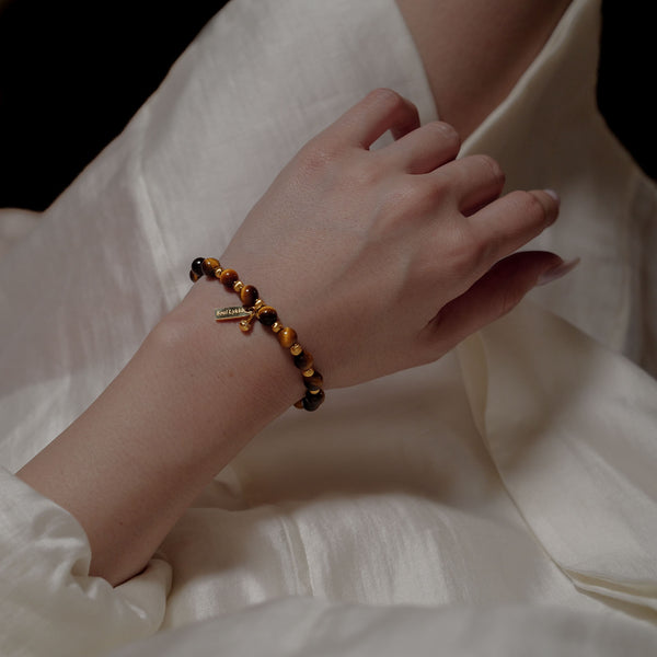 Close-up of the 6mm Tiger's Eye bracelet worn on a woman's wrist. The protective gemstone is aligned with the Solar Plexus and Root chakras to quiet mental noise and anchor effortless composure.