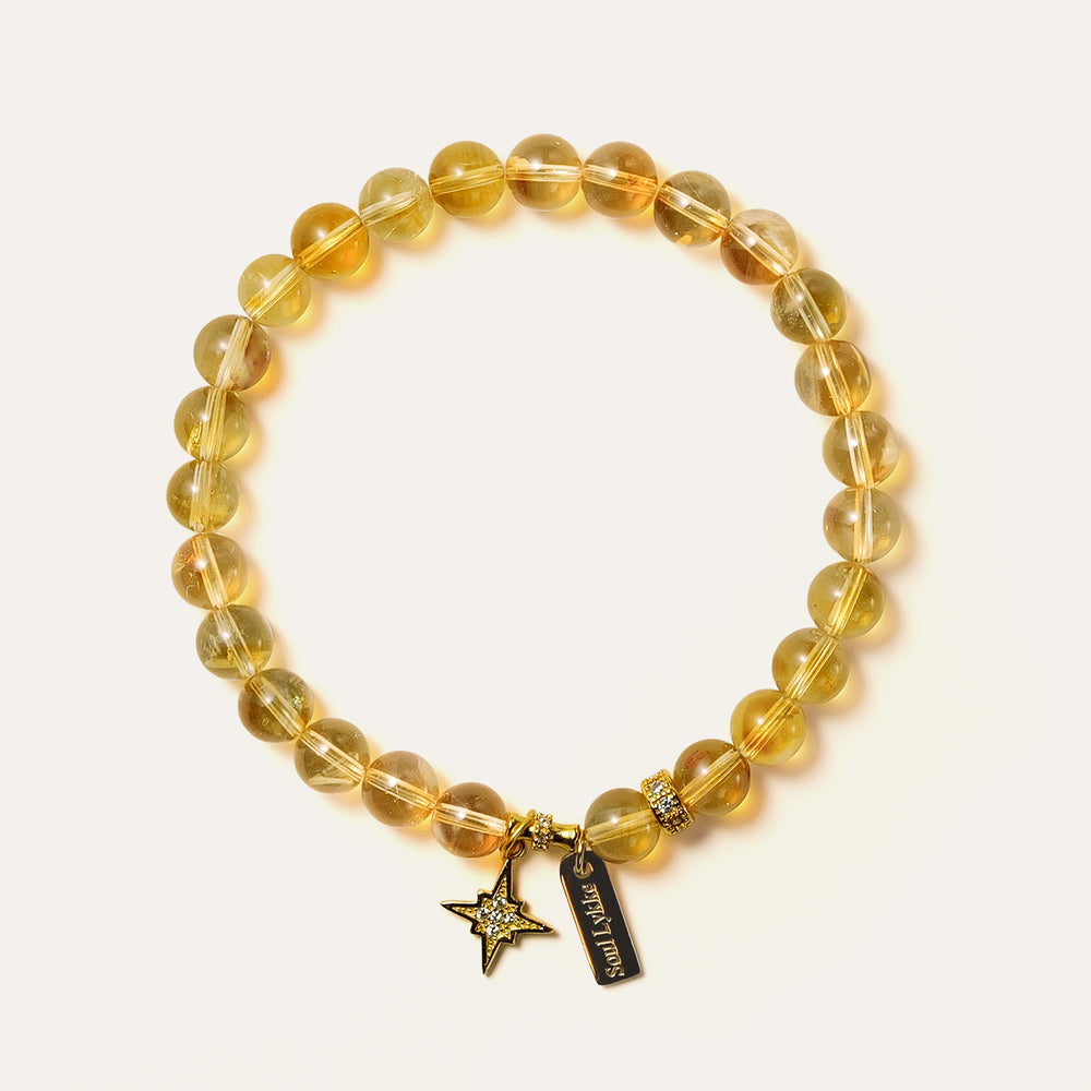 Top-down view of the Soul Lykke Guiding Star bracelet on a neutral background, featuring 6mm AAA Brazil Citrine beads, a 24k gold-plated North Star charm with CZ-pavé accents, and a 14K gold PVD signature tag. This is a natural gemstone and healing crystal bracelet by Soul Lykke.