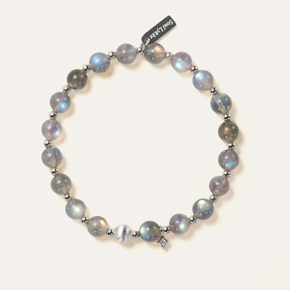 Top-down view of the Soul Lykke Inner Universe bracelet, featuring 6.5-7mm natural AAA-grade Madagascar Labradorite with vivid spectral flashes, accented by 925 sterling silver hardware and a white gold PVD surgical steel tag. This is a natural gemstone and healing crystal bracelet by Soul Lykke.