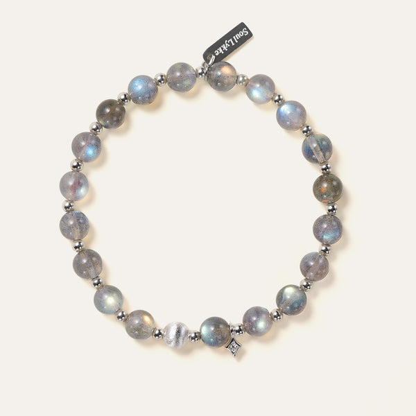 Top-down view of the Soul Lykke Inner Universe bracelet, featuring 6.5-7mm natural AAA-grade Madagascar Labradorite with vivid spectral flashes, accented by 925 sterling silver hardware and a white gold PVD surgical steel tag. This is a natural gemstone and healing crystal bracelet by Soul Lykke.
