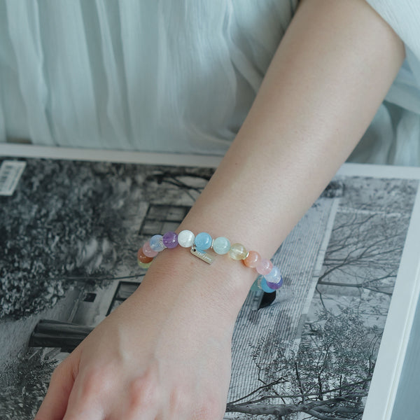 Top view of the Soul Lykke Monet pastel multi-gemstone bracelet on a magazine, featuring 8mm AAA Aquamarine, Amethyst, and Peach Moonstone.