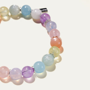 Macro detail of The Monet pastel gemstone bracelet by Soul Lykke, highlighting the hypoallergenic 316L surgical steel signature tag finished in premium white gold PVD. The luminous natural crystals cast delicate colorful shadows, perfectly capturing a serene watercolor aesthetic.
