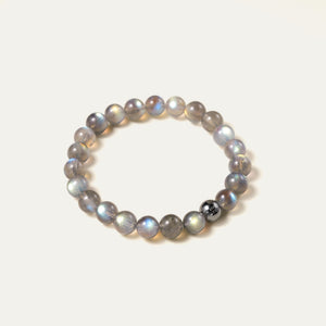 Close-up of the pure labradorite gemstone beads, capturing the silky cat-eye sheen and spectral light of sunset orange and golden hues. Anchored by a white gold PVD signature bead, this stone of magic shields your aura from negative energy.