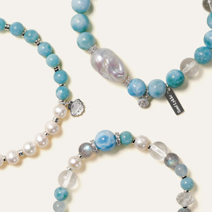 Close-up of three Marine Tear Larimar and freshwater pearl bracelets highlighting the intricate 925 sterling silver seashell charms with CZ accents.