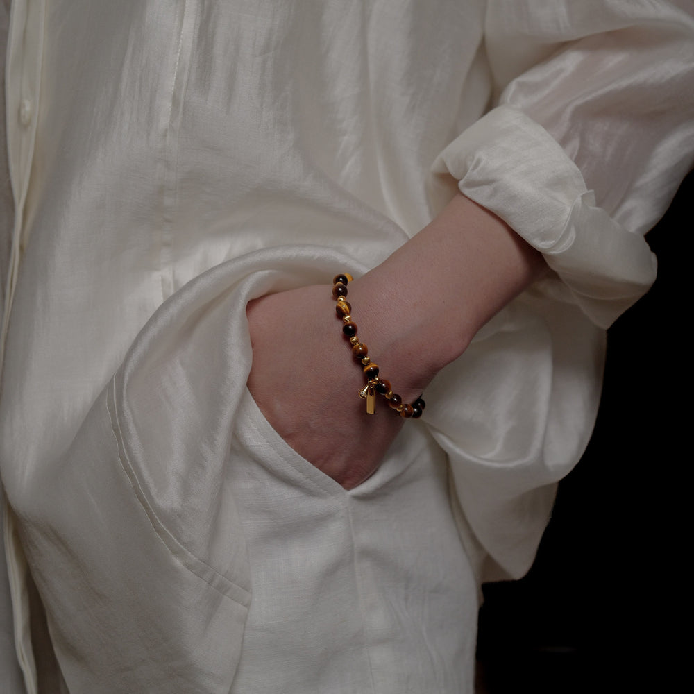 The Golden Glaze bracelet by Soul Lykke, featuring 6mm natural AAA South African Tiger's Eye beads and a delicate 24K gold-plated teardrop charm on a neutral background. This is a natural gemstone and healing crystal bracelet by Soul Lykke.