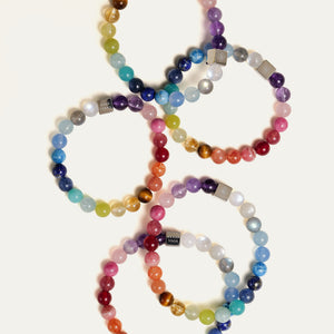 A stunning arrangement of multiple Earth’s Palette bracelets, illustrating the unique chromatic gradient of 25 natural gemstones in each piece. An ultimate luxury blessing gift representing grounded courage, openhearted love, and quiet inner peace.