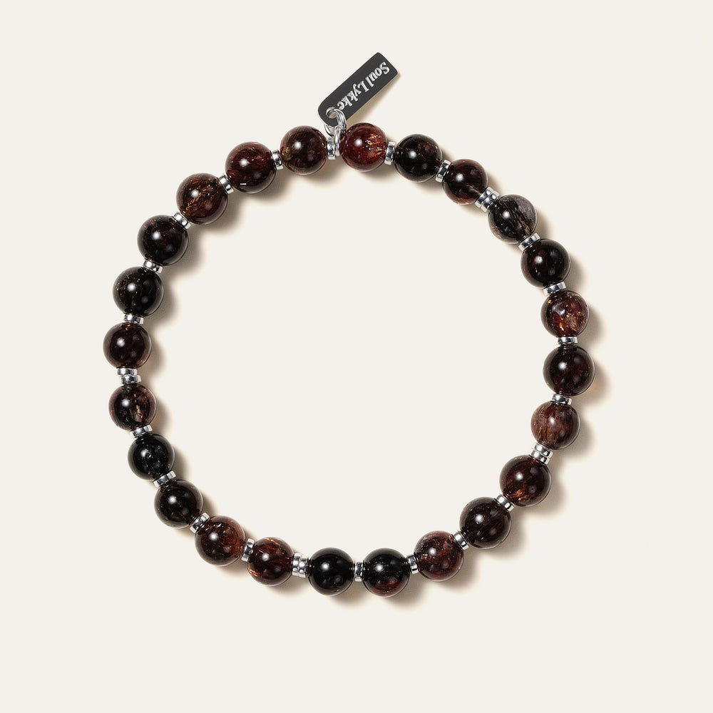 The Eclipse Gold bracelet by Soul Lykke in natural light. Featuring collector-grade 6mm AAA Black Gold Super Seven and high-polished 925 sterling silver spacers, this piece commands an enigmatic, near-solid black presence for understated luxury. This is a natural gemstone and healing crystal bracelet by Soul Lykke.