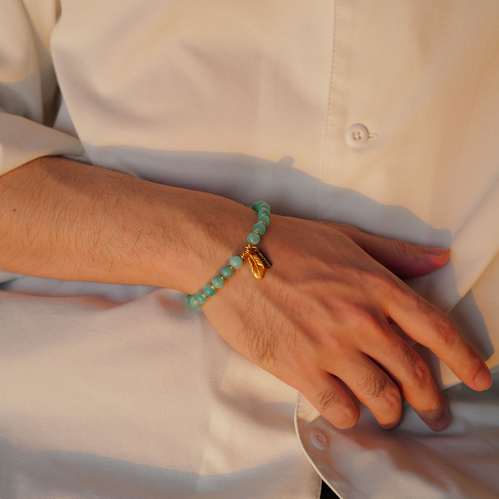 The Tide & Feather bracelet by Soul Lykke, featuring 7mm natural AAA Mozambique icy amazonite beads and a 24K gold-plated sculpted feather charm on a seamless neutral background. This is a natural gemstone and healing crystal bracelet by Soul Lykke.