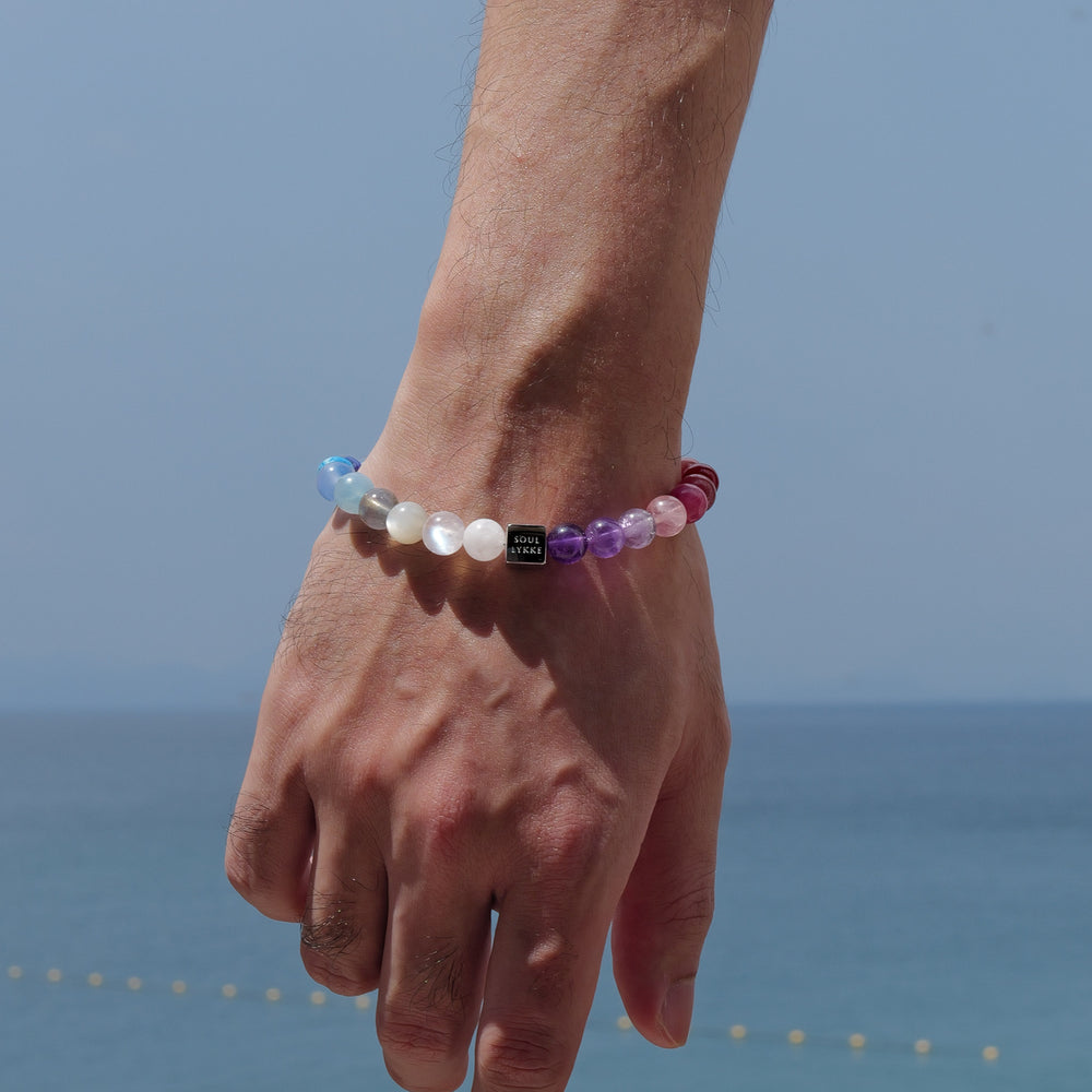The Earth’s Palette flagship bracelet by Soul Lykke. A museum-grade wearable mineral collection featuring 25 distinct 8mm natural gemstones arranged in a seamless chromatic rainbow gradient, accented by a white gold PVD square signature bead. This is a healing crystal bracelet by Soul Lykke.